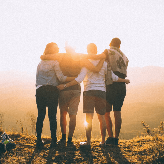 Four people watching a sunset standing arm-in-arm with one another.