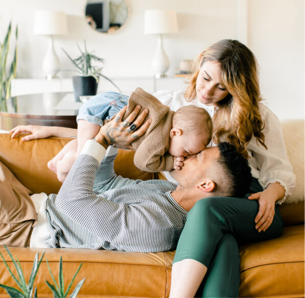 A young couple sitting on their couch and playing with their baby.