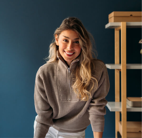 A woman in a brown sweater stands over a desk smiling