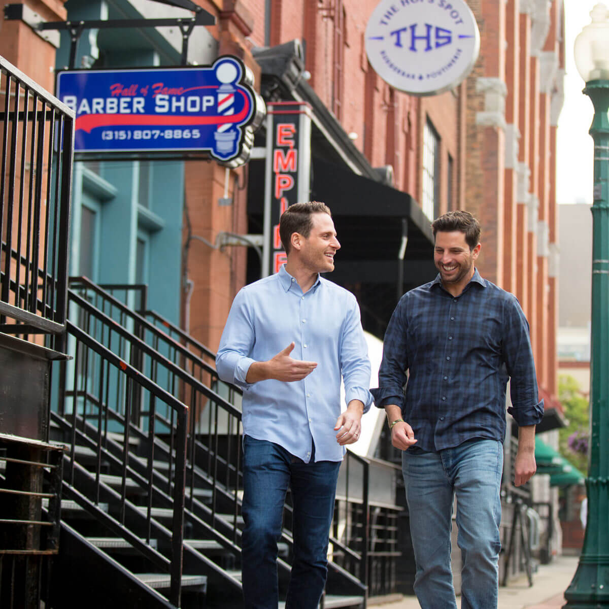 Two men walk down a city sidewalk talking.