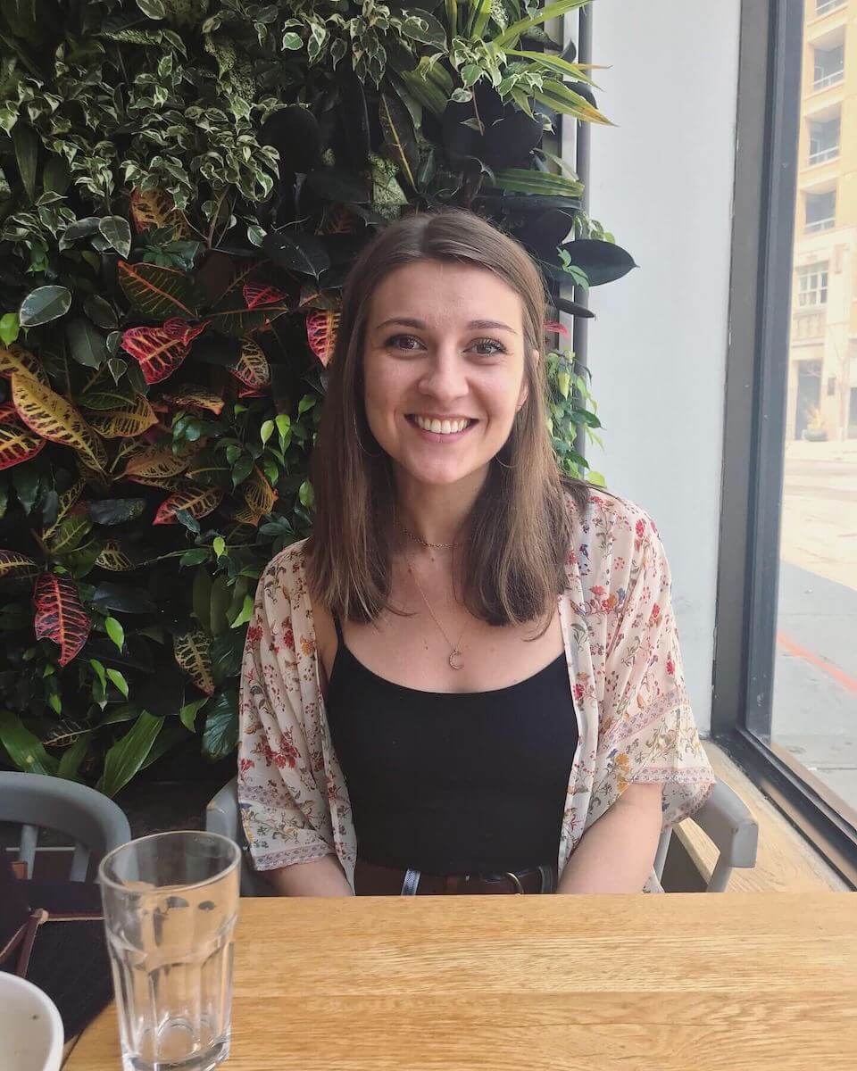 Bridget Doherty wearing black shirt and white cardigan sitting in front of a leafy backgrounds