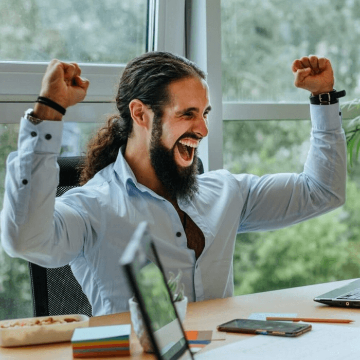 Man sitting at an office table has his hands in the air in celebration.