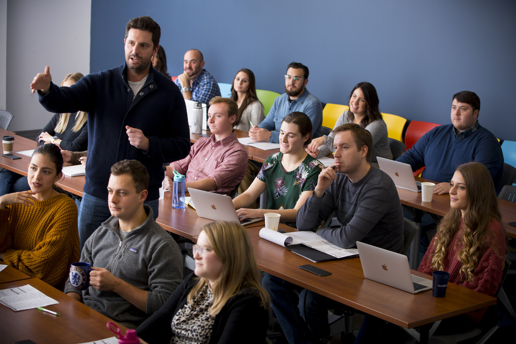 Man points and speaks in a room of people listening.