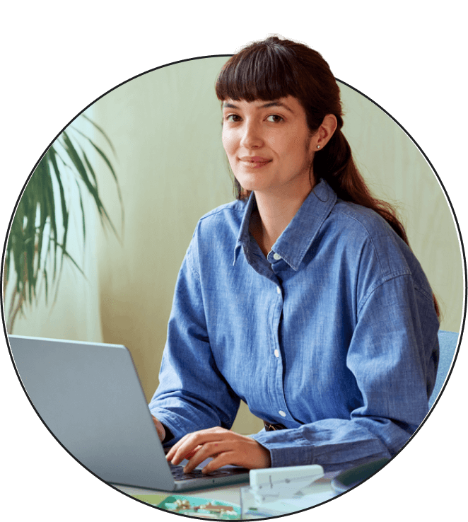 A brunette woman looking straight ahead while sitting and working on a laptop.