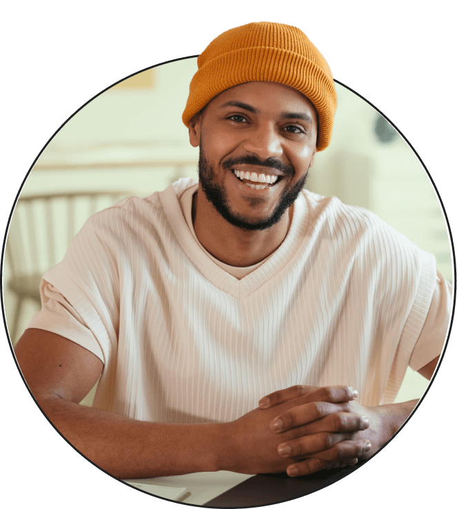 A young man with a hat on smiling a looking straight ahead.