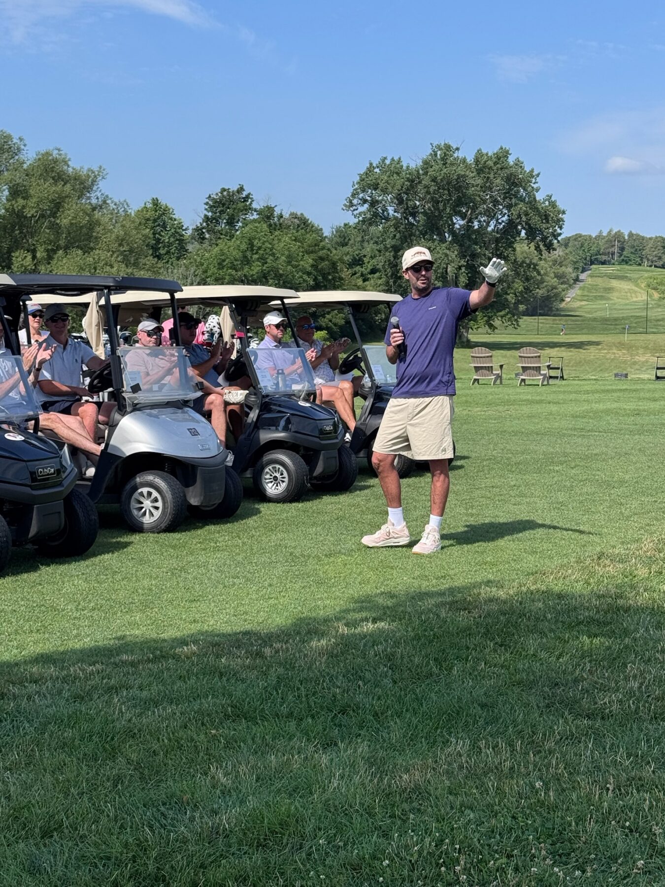 A man stands in front of several golf carts making a speech to golfers