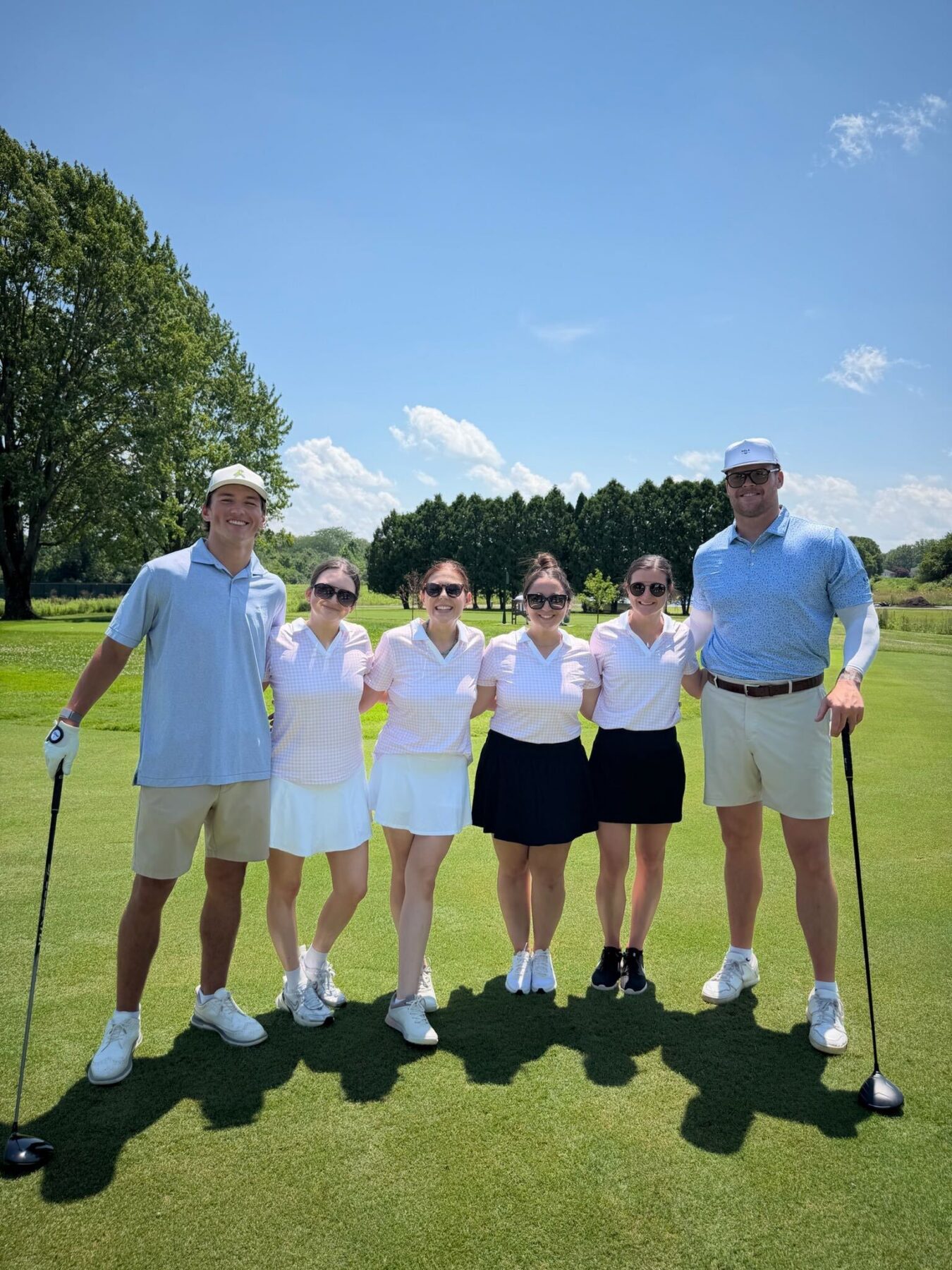 Two men and four women golfers smile on a golf course
