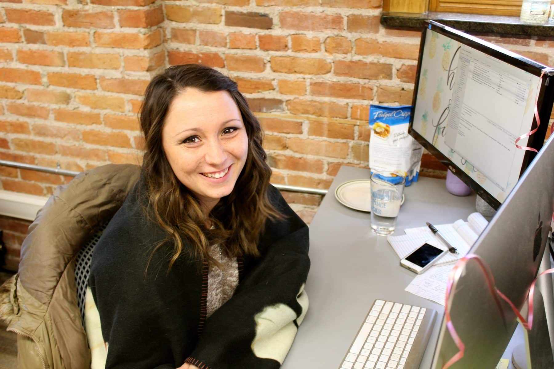 A woman, sitting a desk, smiles at the camera