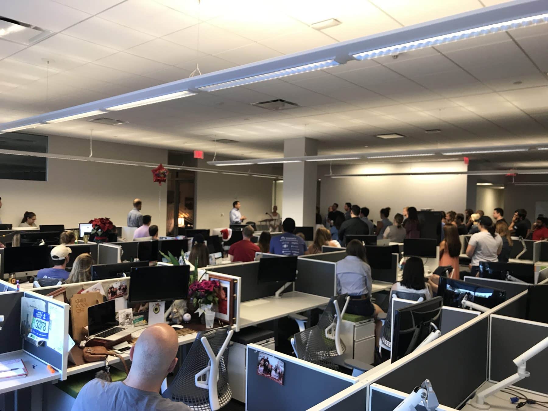 Workers sit in an open office envirornment, listening to a man speak