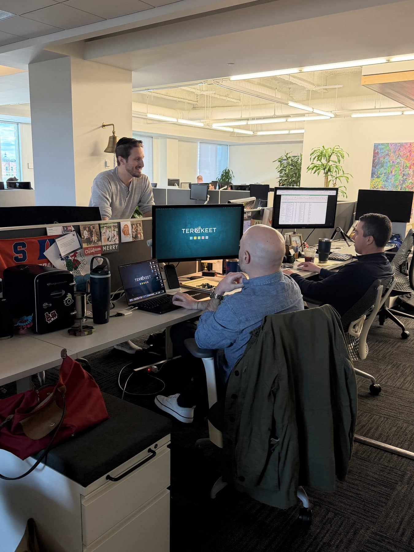 Three men smile and talk in the Terakeet office