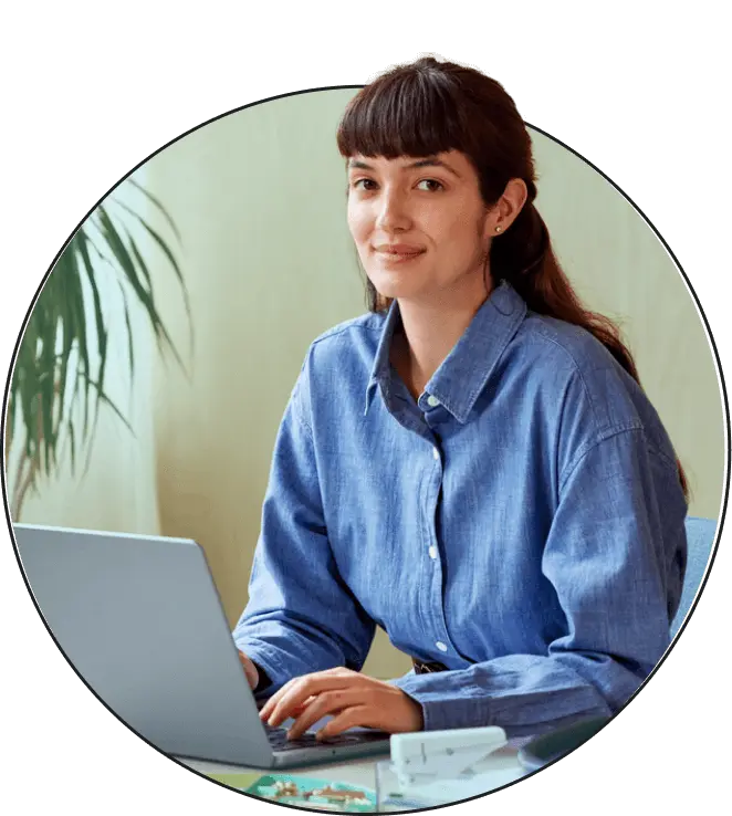 A brunette woman looking straight ahead while sitting and working on a laptop.