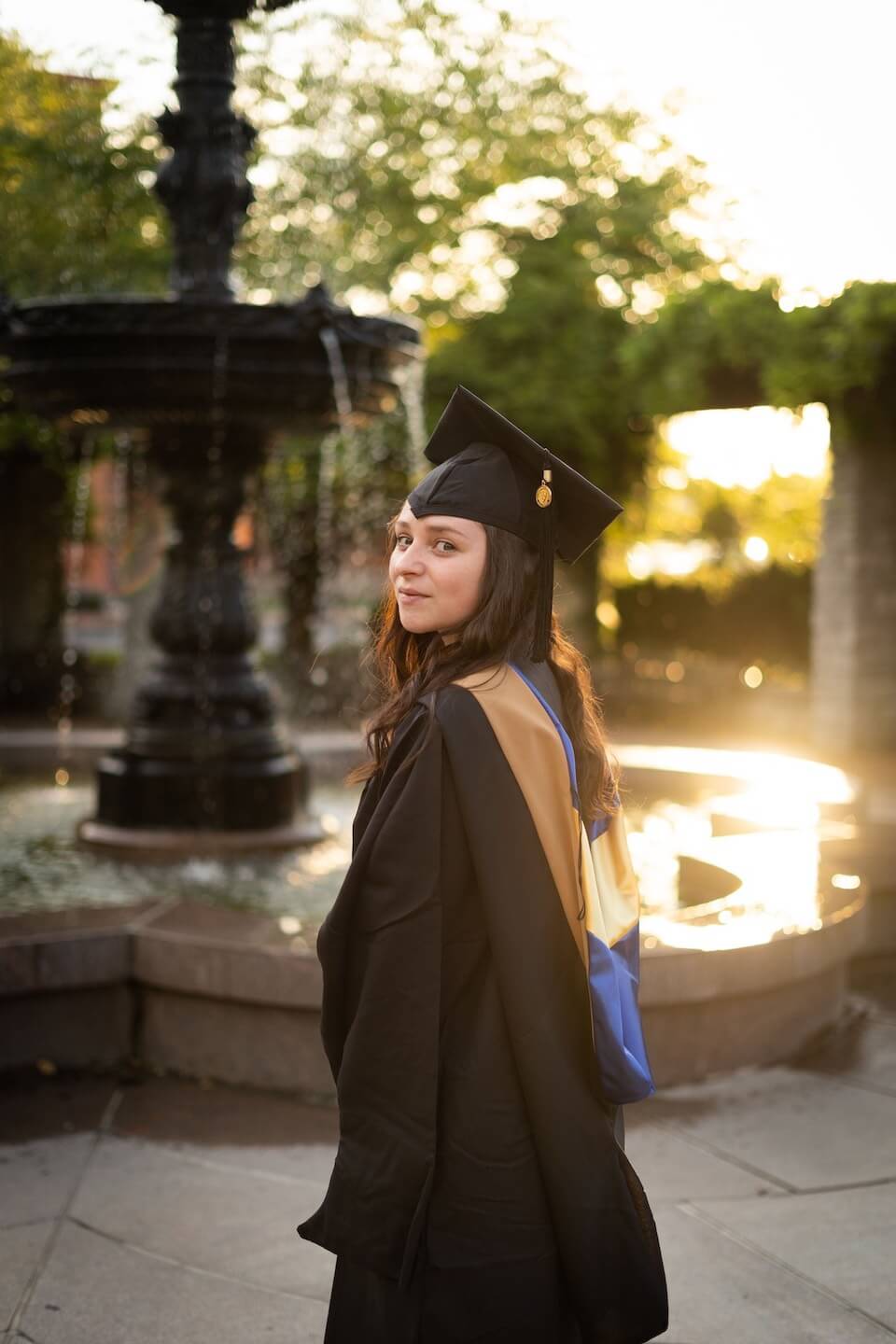 Monica Bennett standing in front of fountain in graduation cap and gown