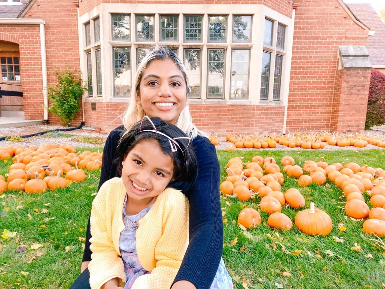 Supriya Venkatesan sits in front of some fall pumpkins and shares a hug with her daughter.
